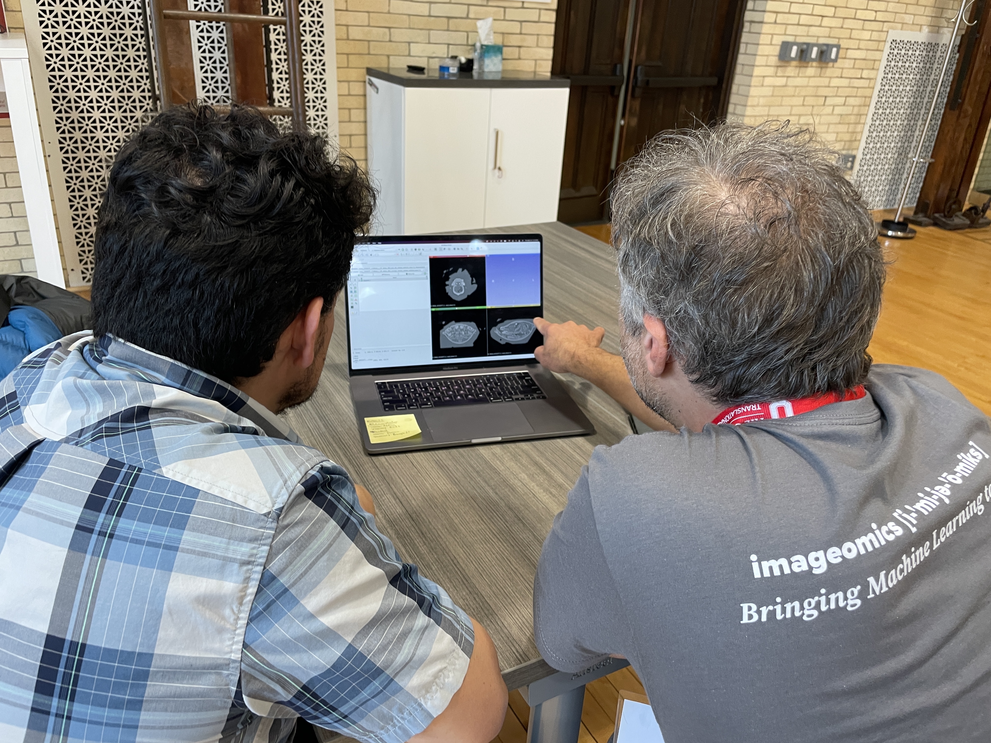 Two researchers view biological scans on a laptop. The one on the right wears a grey "imageomics" shirt and points at the screen.